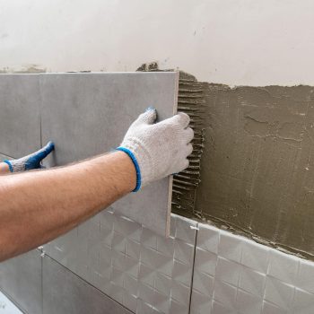 The hands of the tiler are laying the ceramic tile on the wall. Horizontal image. Close up.